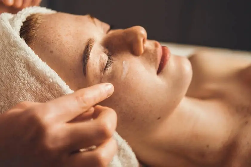 Esthéticienne réalisant un soin de visage à domicile, avec des produits de soin professionnels, illustrant un moment de détente et de bien-être ; soin visage, soin de visage et soin cheveux inclus dans la routine beauté.